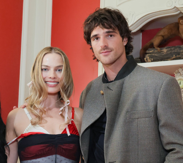 Margot Robbie appears with Jacob Elordi. She wears small pale pink bows in her hair.